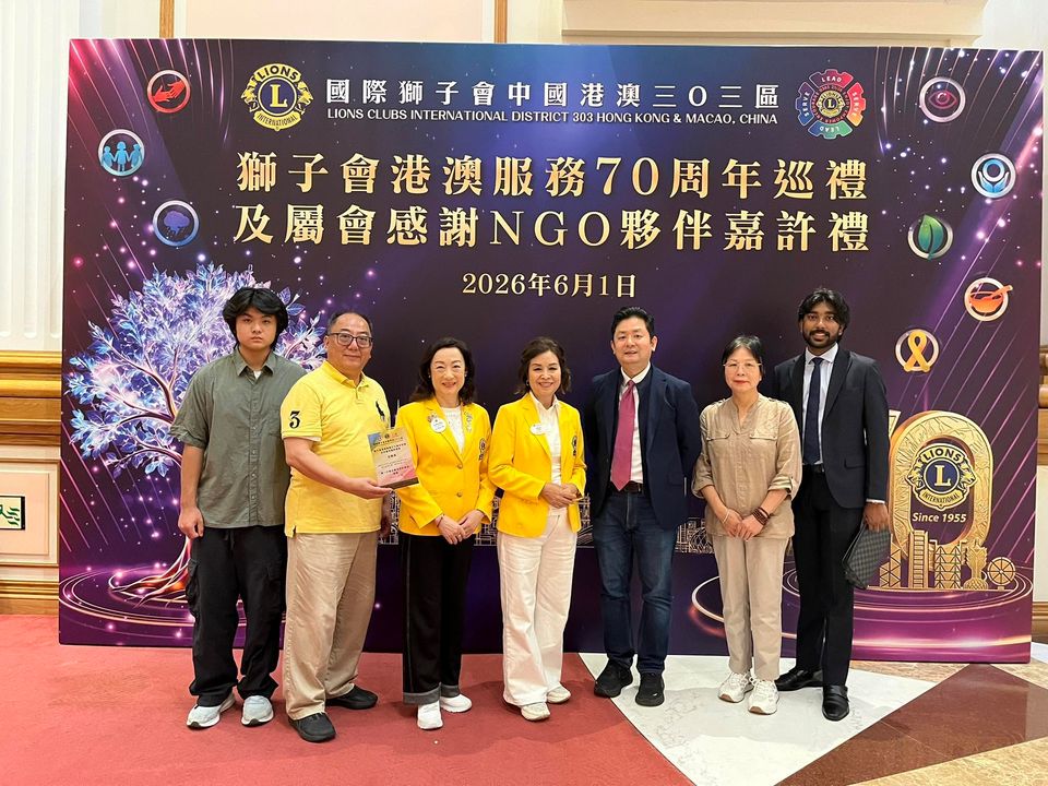 七個人站在獅子會70周年典禮的背景板前,其中一人手持一塊嘉許牌匾。