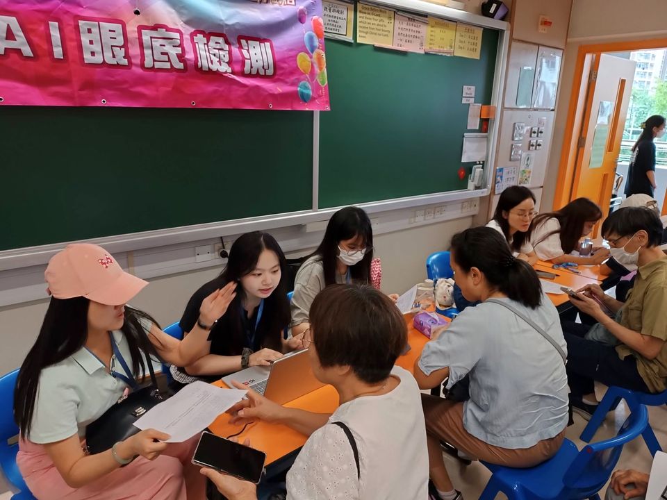 年輕義工和年長的訪客坐在橙色桌子旁，對著列印出來的紙張交談。